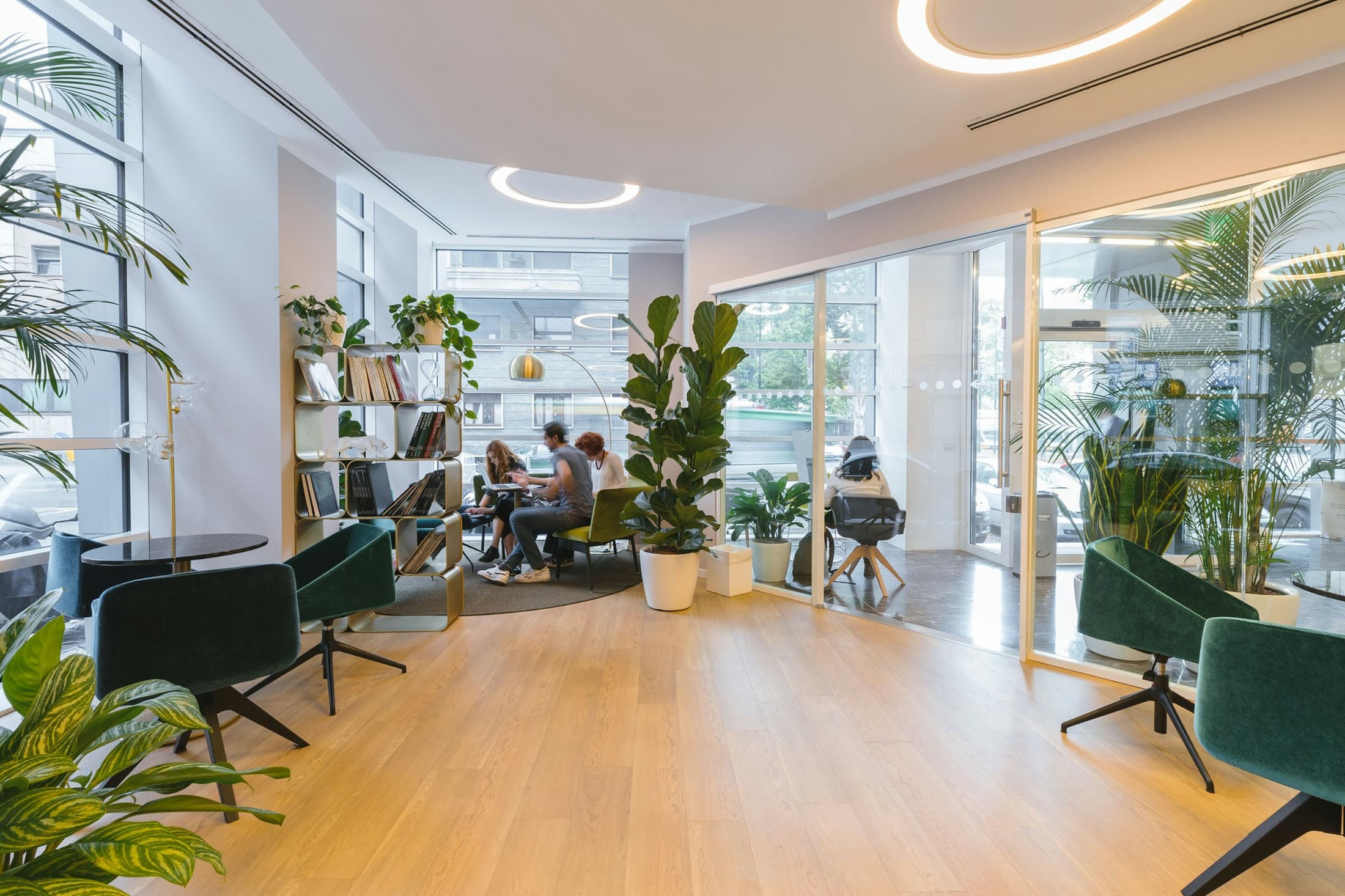 Modern office lounge with grey seating, wood floors, and tall windows